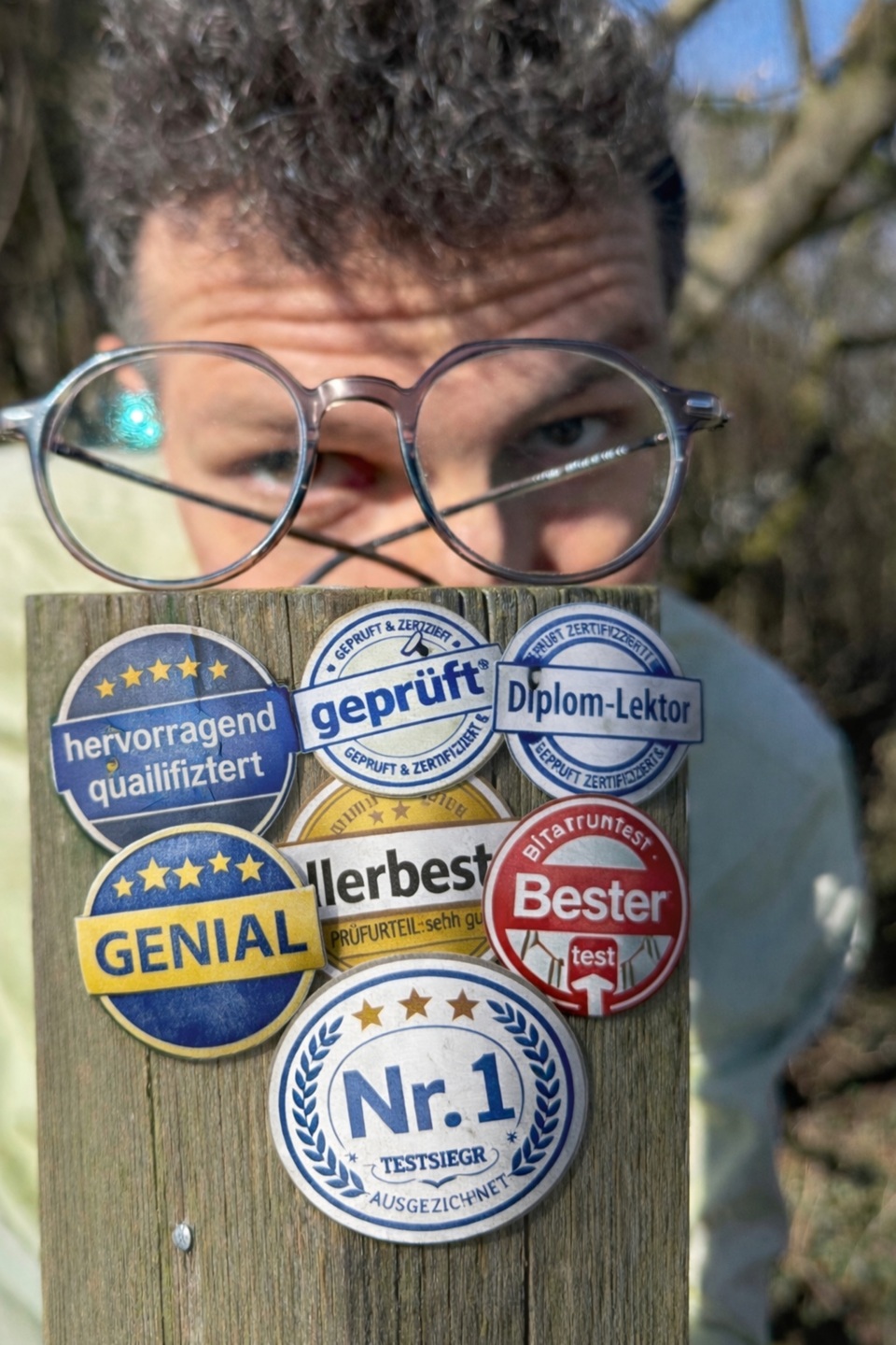 Der Lektorenausbilder Evgenij Unker vor einem Pfahl mit Plaketten. Diese sind mit KI erstellt und existieren in Wirklichkeit nicht.